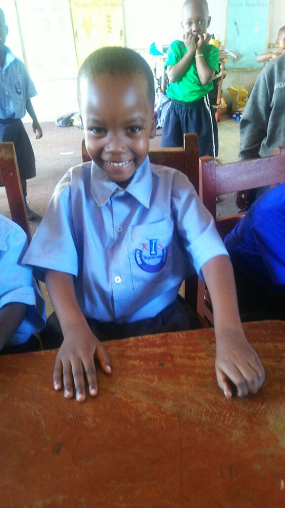 Smiling student in Karibu International School uniform at his classroom desk